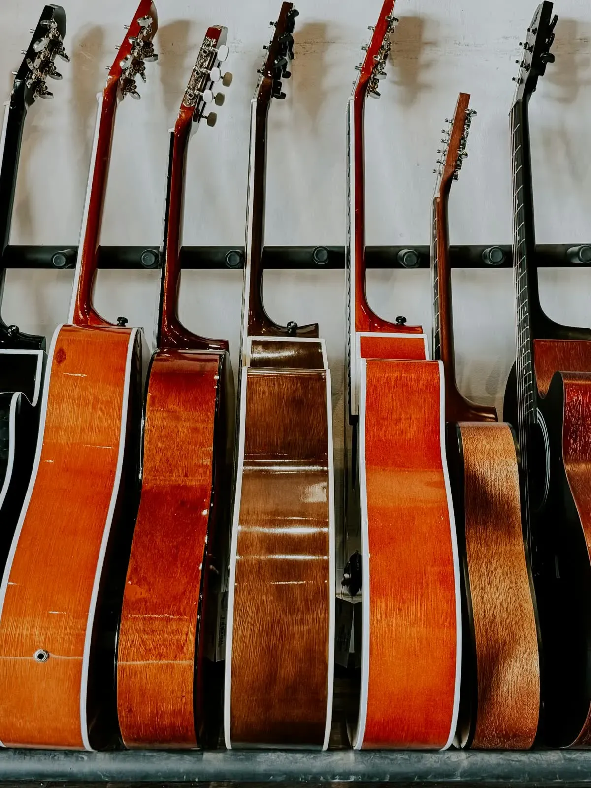 Rangée de guitares acoustiques posées sur un présentoir, vues de côté