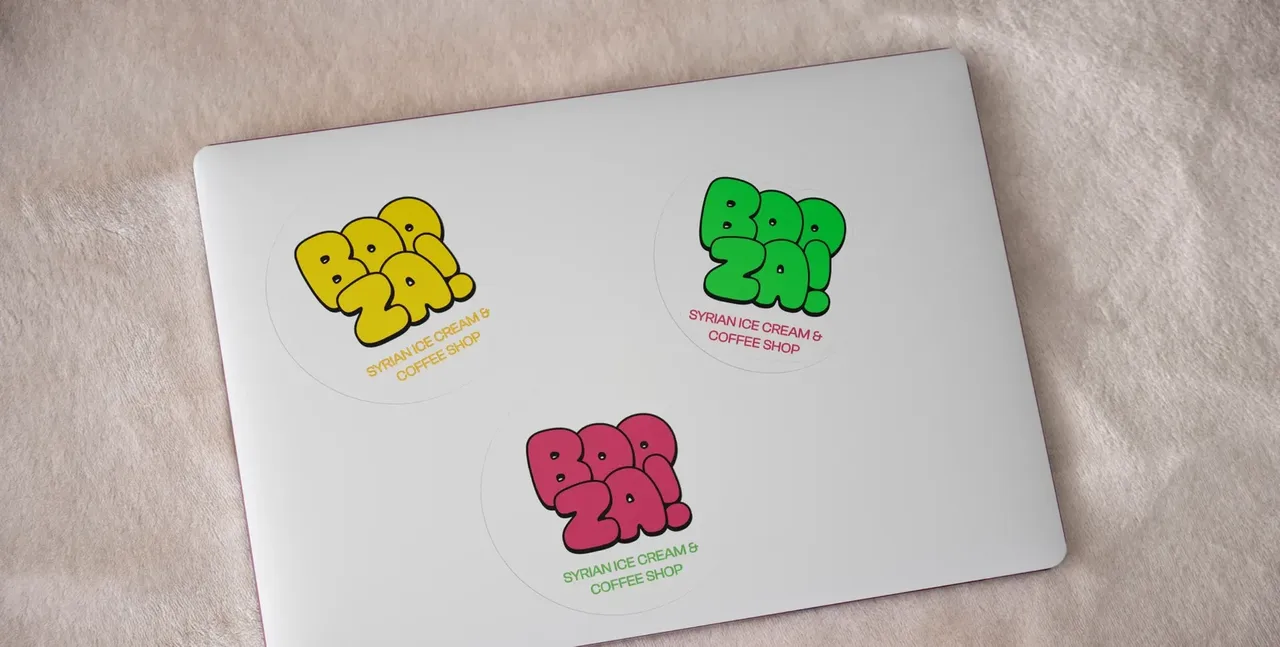 Capot d'ordinateur portable gris avec trois autocollants ronds Booza!, logo en jaune, en vert et en rose