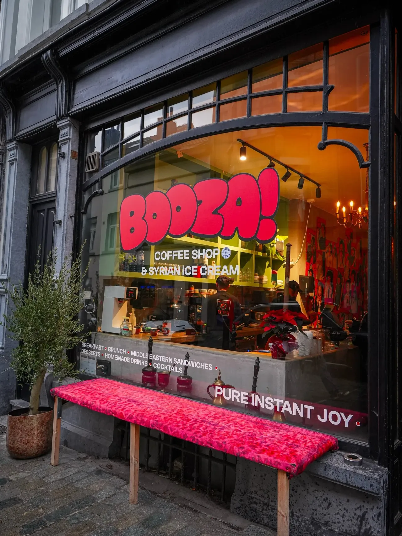 Vitrine du café Booza! de jour, logo rouge, lettrage « Coffee shop & Syrian ice cream » et banc rouge devant la façade