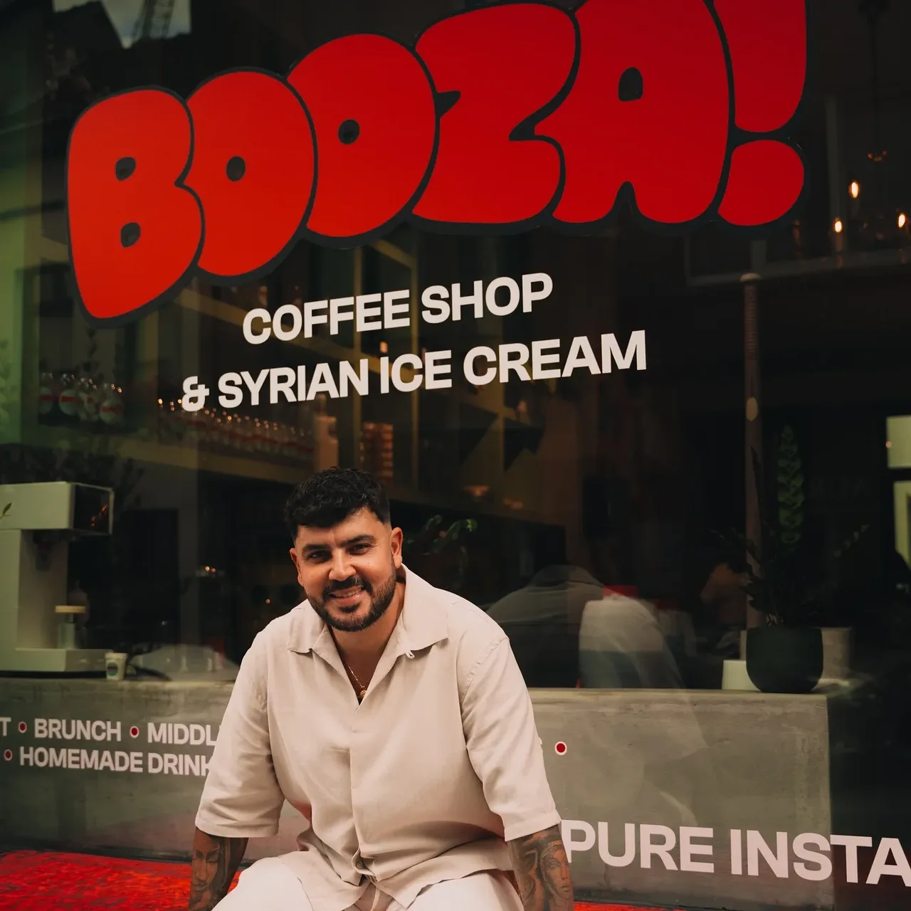 Portrait devant la vitrine Booza!, le logo rouge et le lettrage en grand derrière