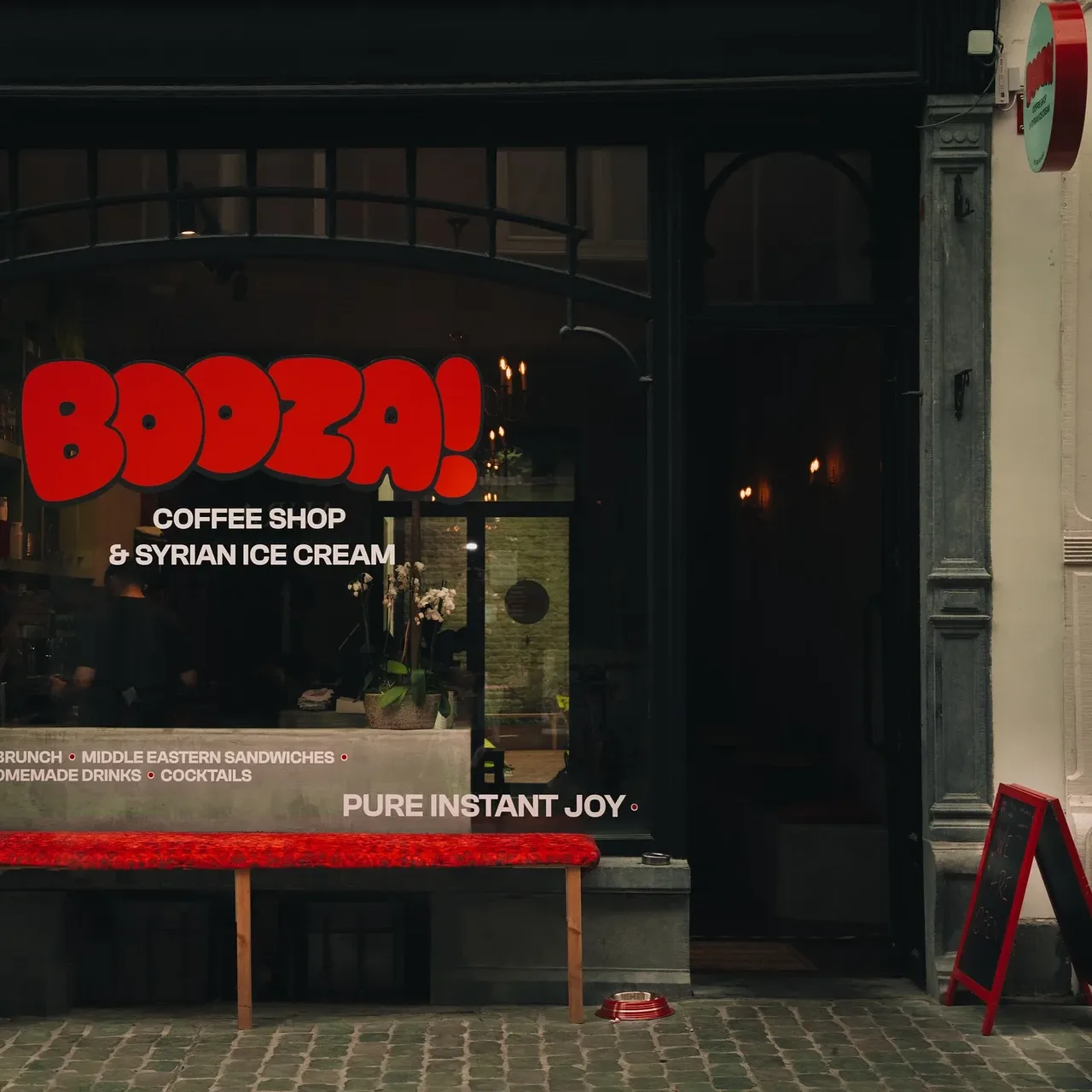 Façade de Booza! vue de face, logo rouge sur la vitrine, banc rouge et chevalet sur le trottoir