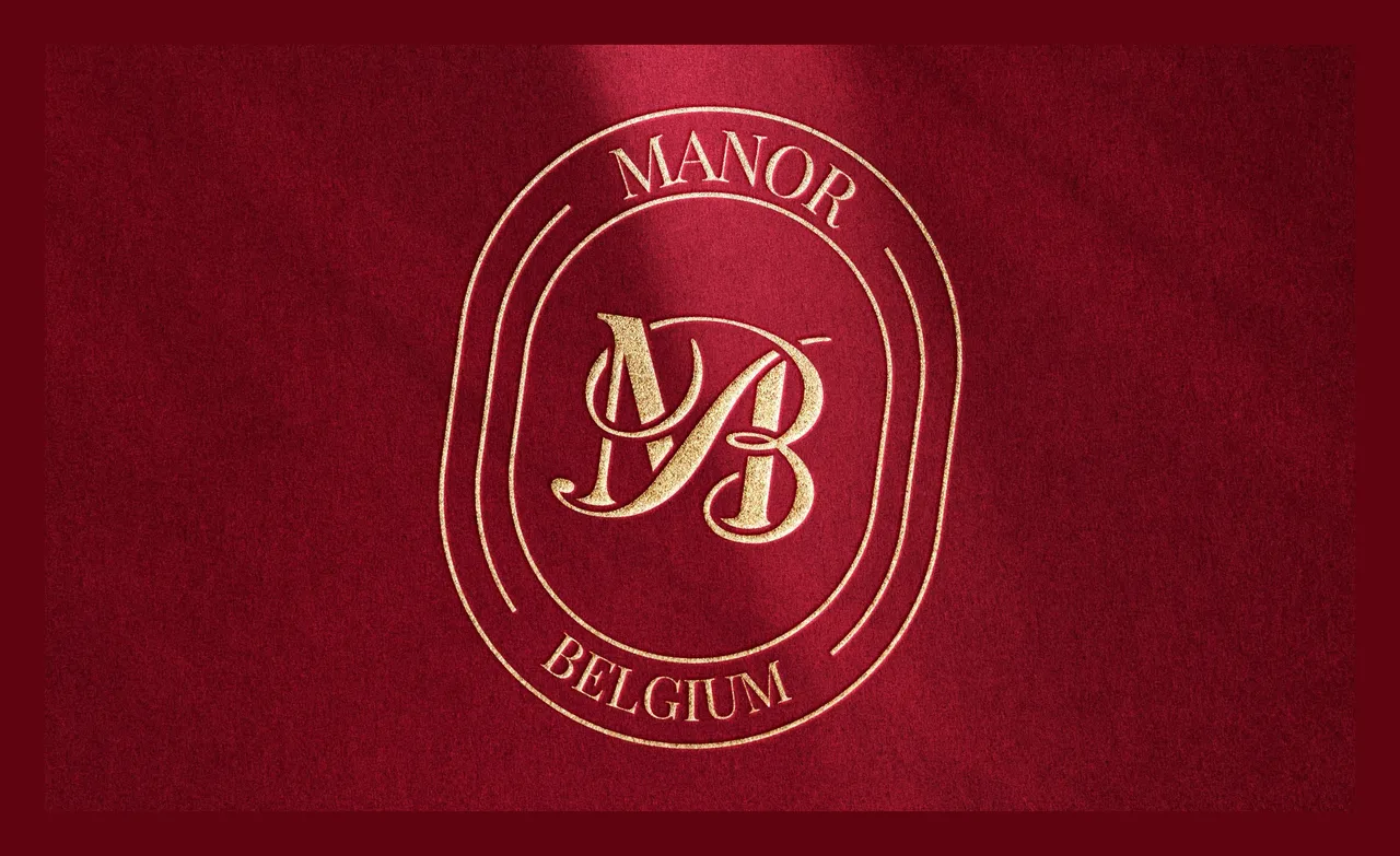 Sceau ovale Manor Belgium doré sur velours rouge, avec le monogramme MB au centre