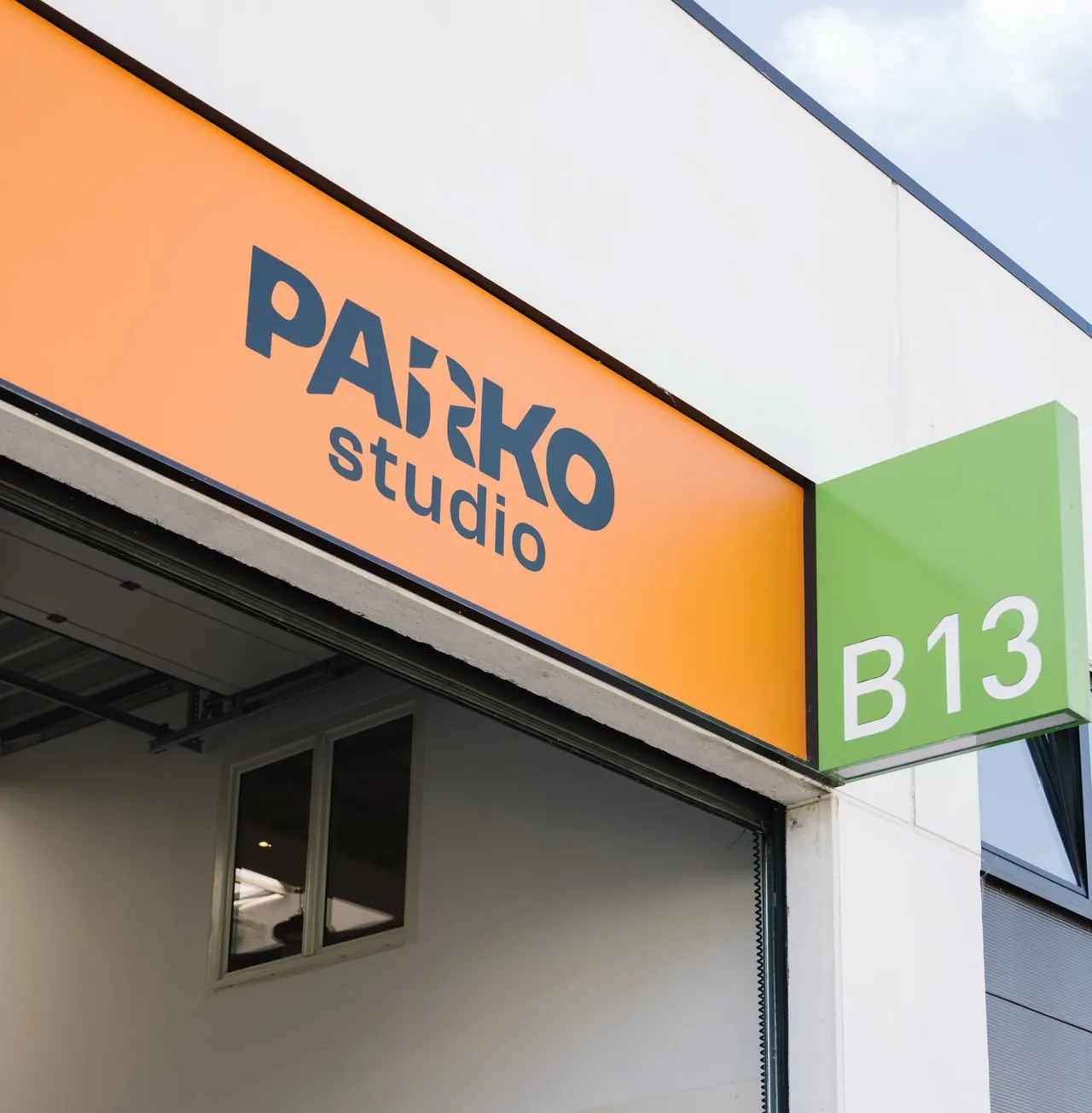 Enseigne orange Parko Studio au-dessus de la porte du studio à Wavre, à côté d'un panneau vert numéroté B13