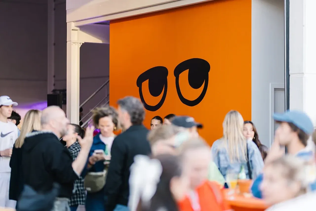 Événement au studio Parko : des invités discutent devant un mur orange où sont peints les grands yeux de la mascotte