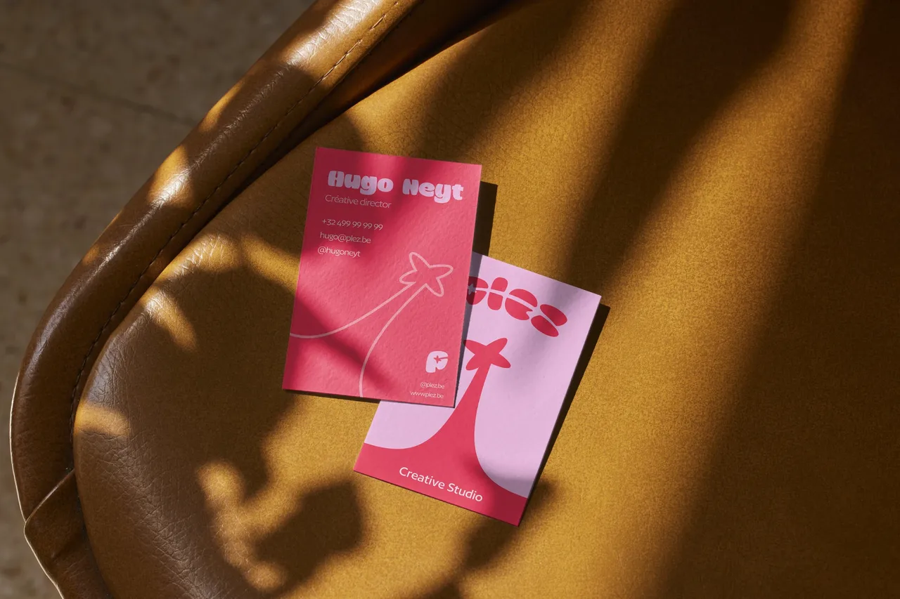 Deux cartes de visite Plez, rose vif et rose pâle, avec l'étoile filante et la mention « Creative Studio », sur un fauteuil en cuir