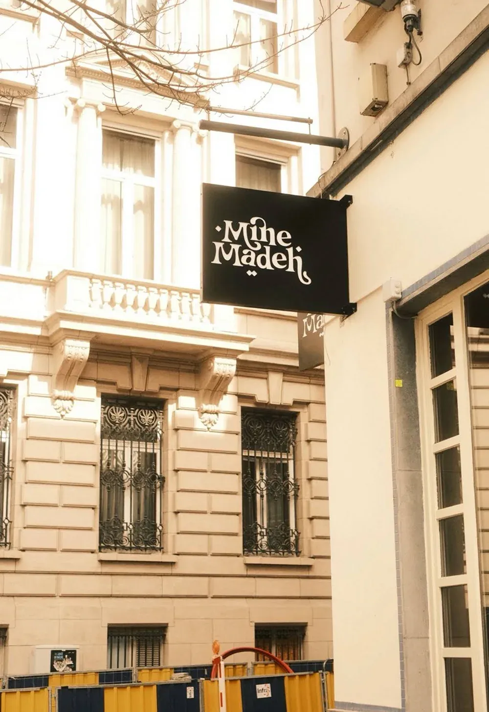 Enseigne drapeau Mine Madeh, logo clair sur fond sombre, accrochée à la façade du restaurant