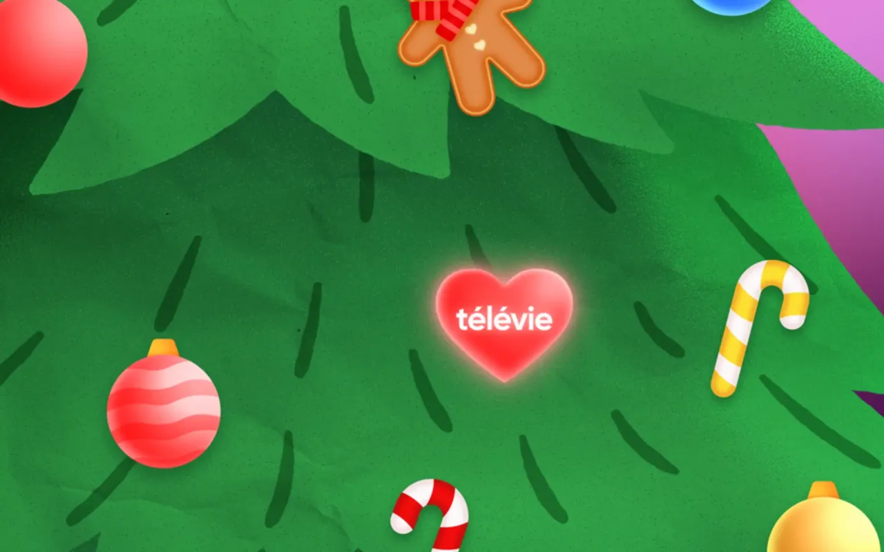 Gros plan sur les branches du sapin : le cœur lumineux Télévie entouré de boules, de cannes à sucre et d'un bonhomme en spéculoos