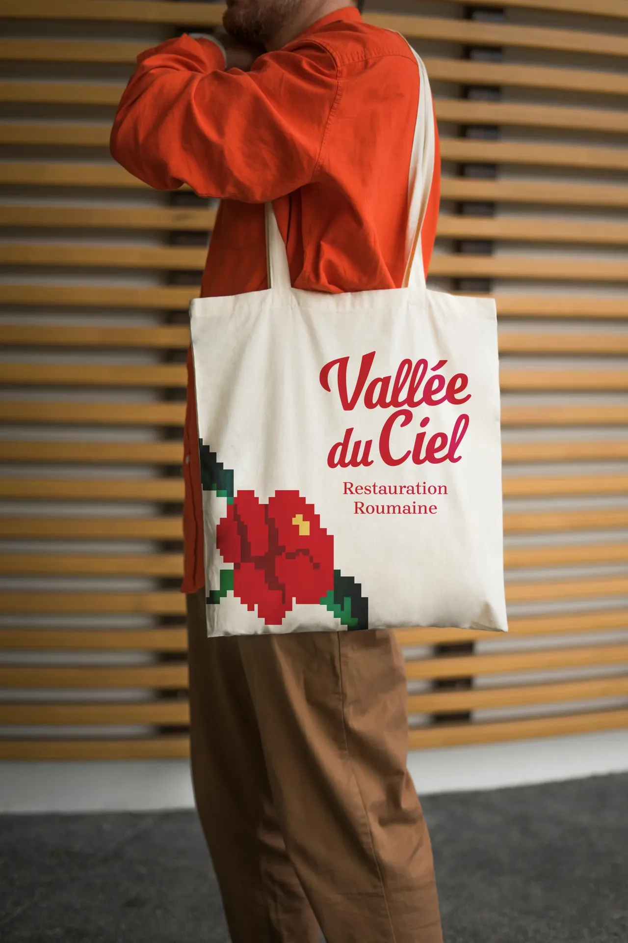 Tote bag écru Vallée du Ciel porté à l'épaule, logo rouge et rose brodée en point de croix dans le coin